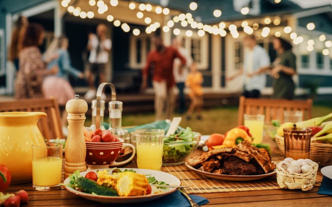 Summer catering ideas - A group of people having an outdoor summer party featuring a table filled with different foods.