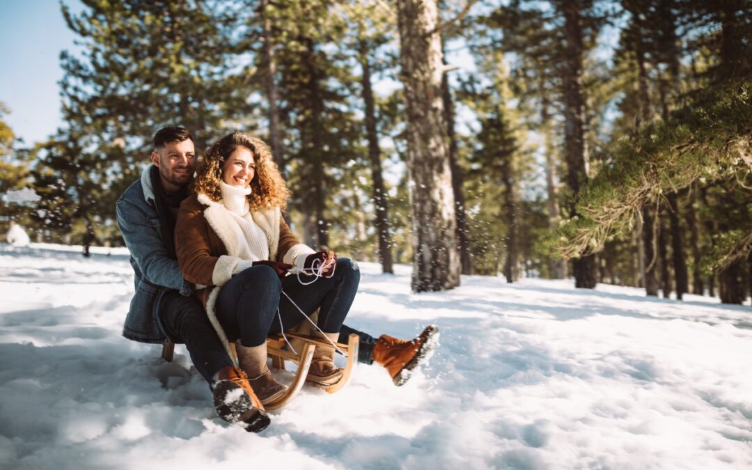 Winter date ideas on Long Island - A couple riding a sled together on a snowy mountain.